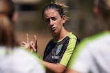 A female coach looks towards her players, while holding her fingers to demonstrate a move.