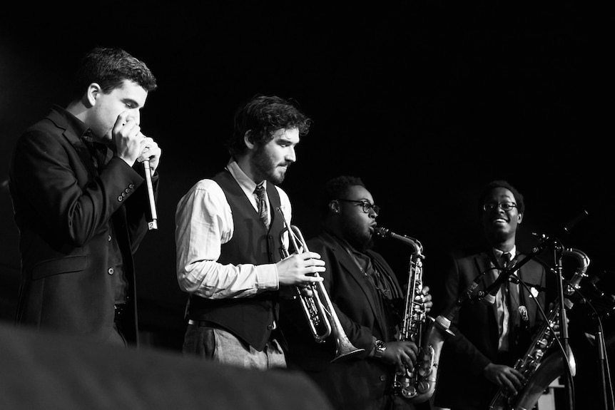 A black-and-white shot of four men playing brass instruments on a stage.