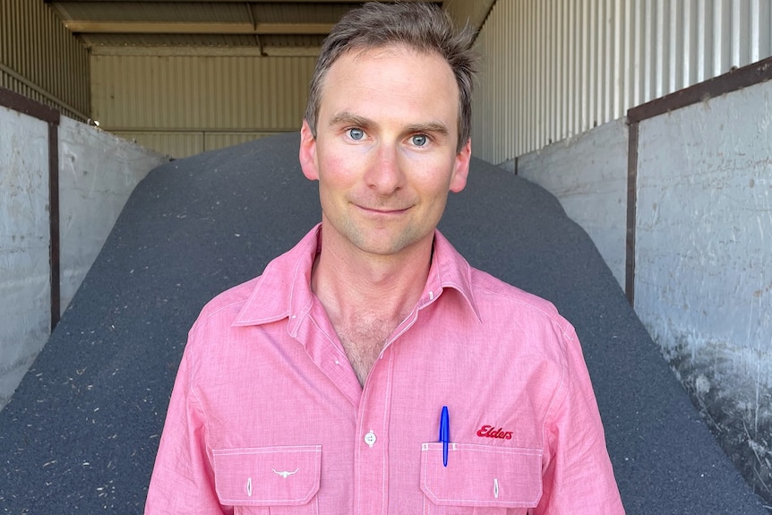 A man wearing a light red shirt stands in front of a mound of fertiliser.