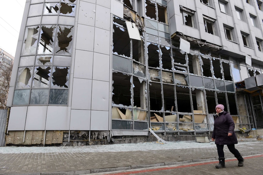 Woman walks past shattered building in Ukraine