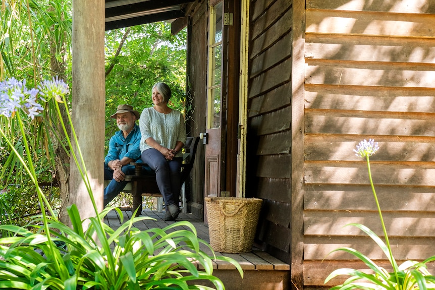 A woman and man sit on a verandah of a cabin.