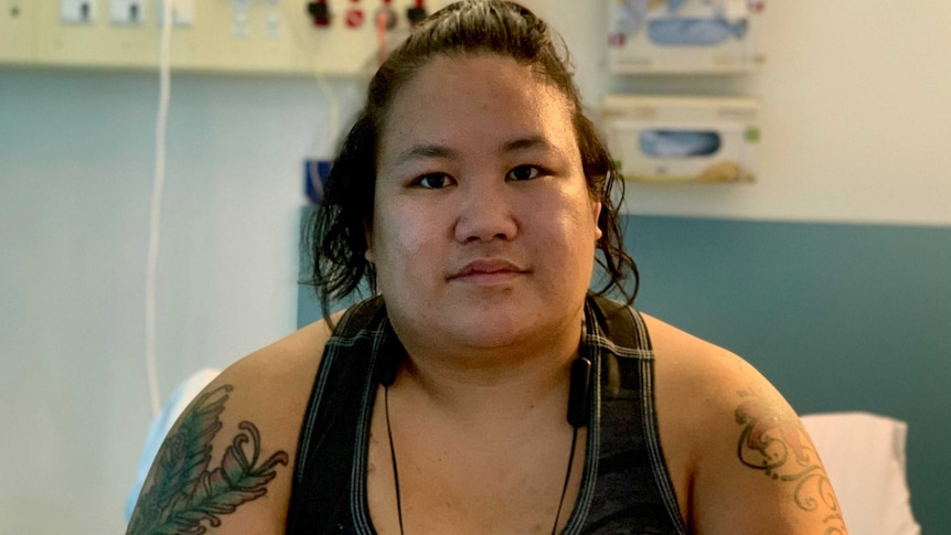 A woman sits in a hospital bed, facing the camera.