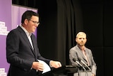 Premier Daniel Andrews stands at a podium addressing the media with Chief Health Officer Brett Sutton to the side.