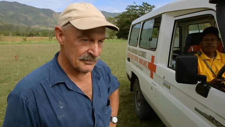 A man stands next to a four wheel drive Ambulance in a forest clearing in PNG.