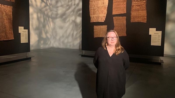 Woman in black in front of large bark fabric with designs.