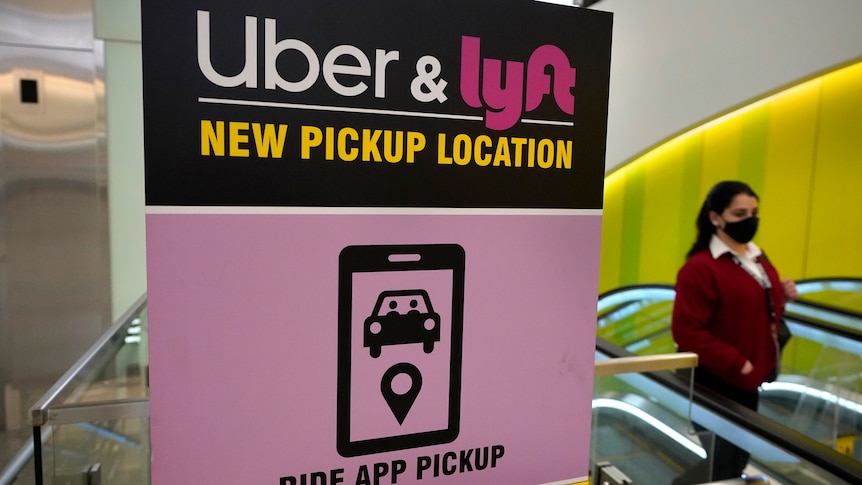 a person stands next to a pink sign providing directions for uber and lyft pickups at an airport in america