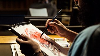 An artist paints an image on a notepad while sitting in a radio studio.