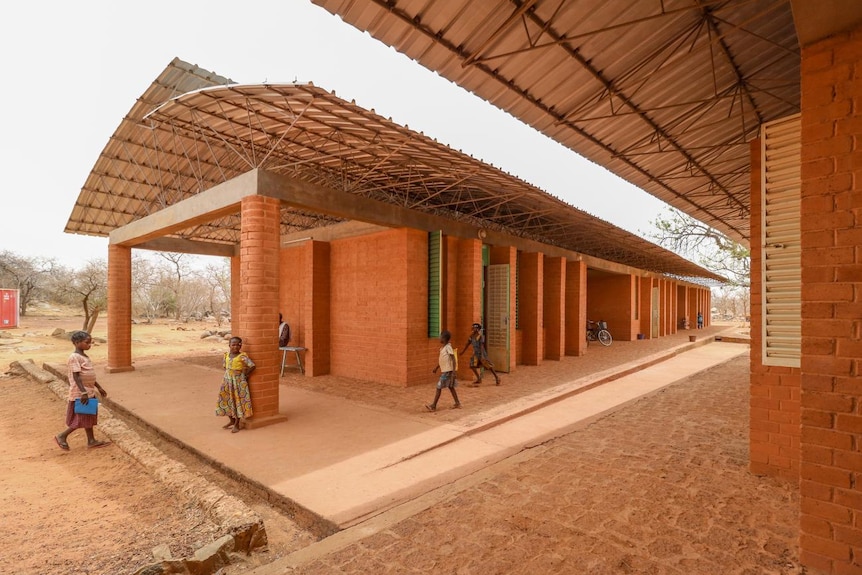 A school in Africa with clay bricks and students walking through corridors.