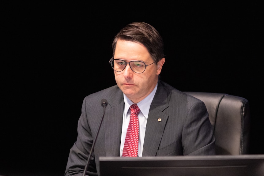 A photo of Alastair McEwin in front of a microphone against a black background.