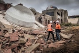 Two workers stand and point at a fallen dome knicked down in the demolition of the Taj on Swan.