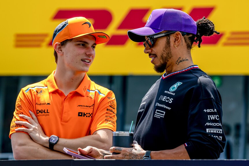 Oscar Piastri talking to Lewis Hamilton before an F1 race, both wearing team polo shirts