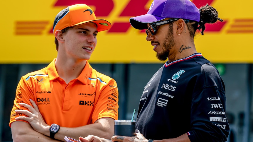 Oscar Piastri talking to Lewis Hamilton before an F1 race, both wearing team polo shirts