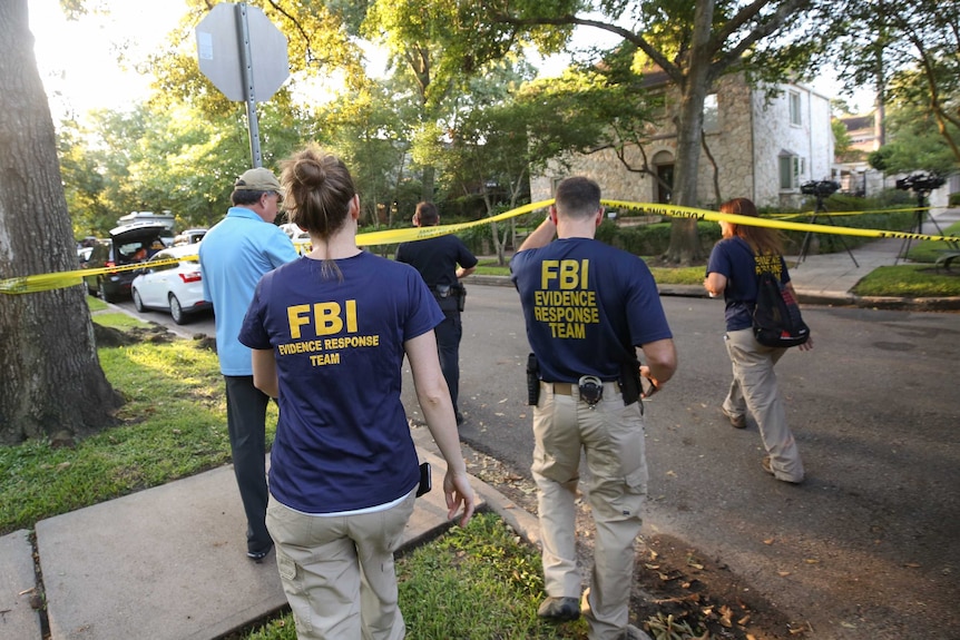 FBI agents walk under police tape.