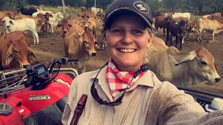 Selfie shot of woman on four wheel drive motorbike in paddock full of cows