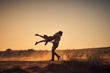 Two dancers in a sunset setting. One  is lifting the other. 
