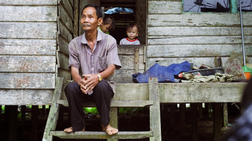 A man wearing a button down shirt and pants sits on the steps of a house.