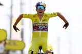Wout van Aert holds his arms out in celebration while riding over the line wearing the yellow jersey