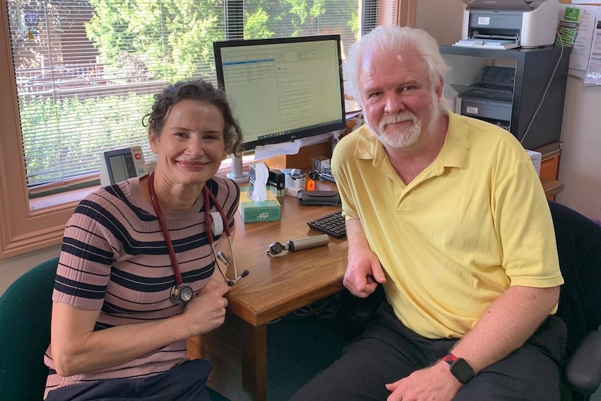 a man and woman smile at the camera at a desk