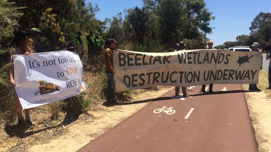 Protestors against the Roe 8 highway project holding banners on a cycle path at Beeliar Regional Park.