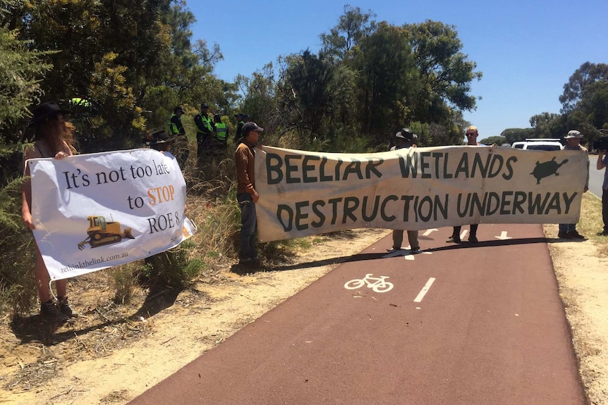 Protestors against the Roe 8 highway project holding banners on a cycle path at Beeliar Regional Park.