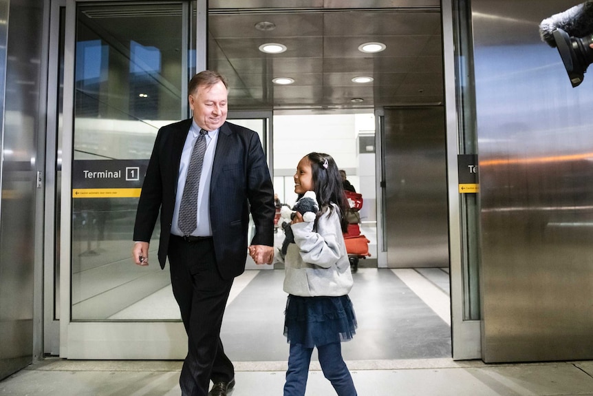 Robert Tibbo holds Keana's hand as they walk through a walk at the airport.