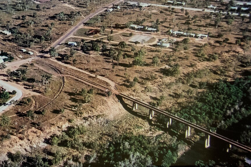 A faded aerial photo showing a a bridge over a dry river bed connecting to a road under construction on the other side.