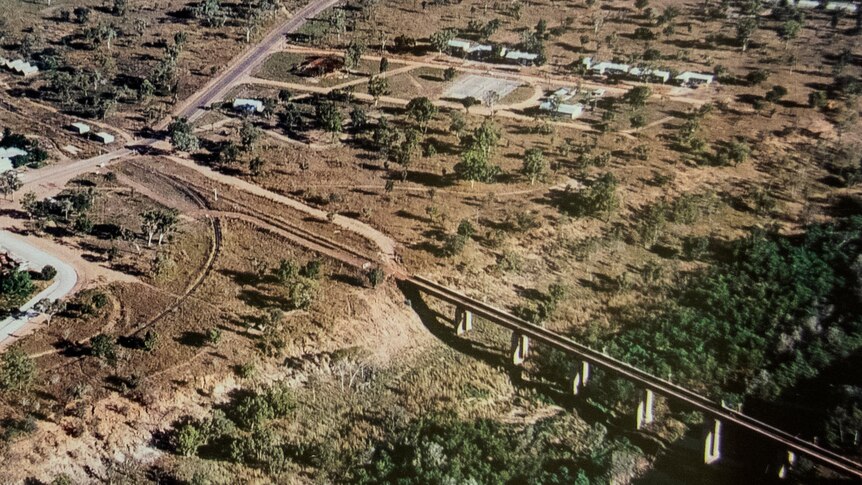 A faded aerial photo showing a a bridge over a dry river bed connecting to a road under construction on the other side.