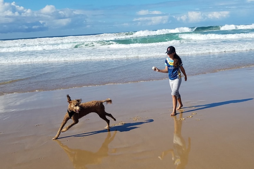 Girl holding a ball with dog running on beach