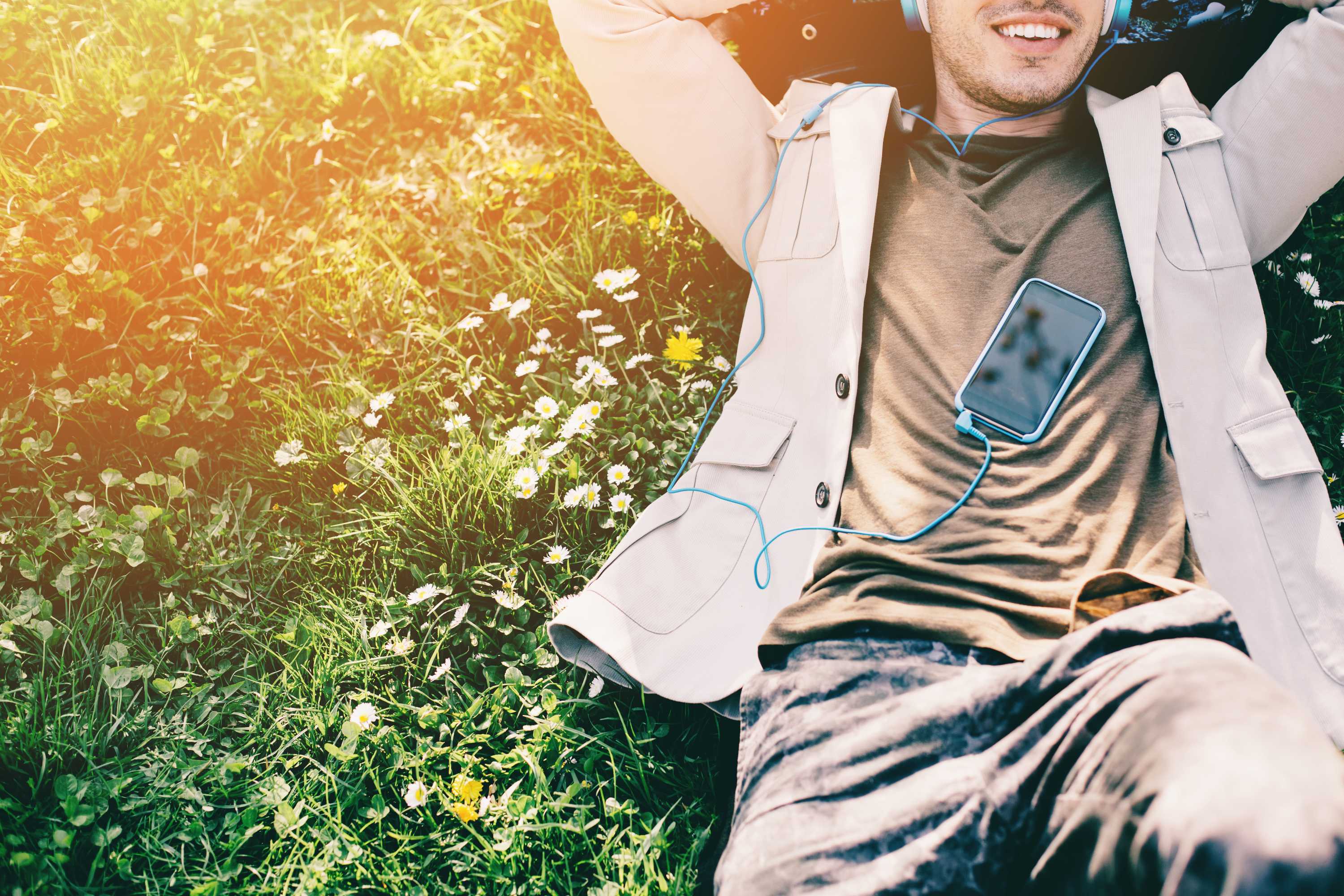 A smiling man wearing headphones plugged into his phone listens to an audiobook.