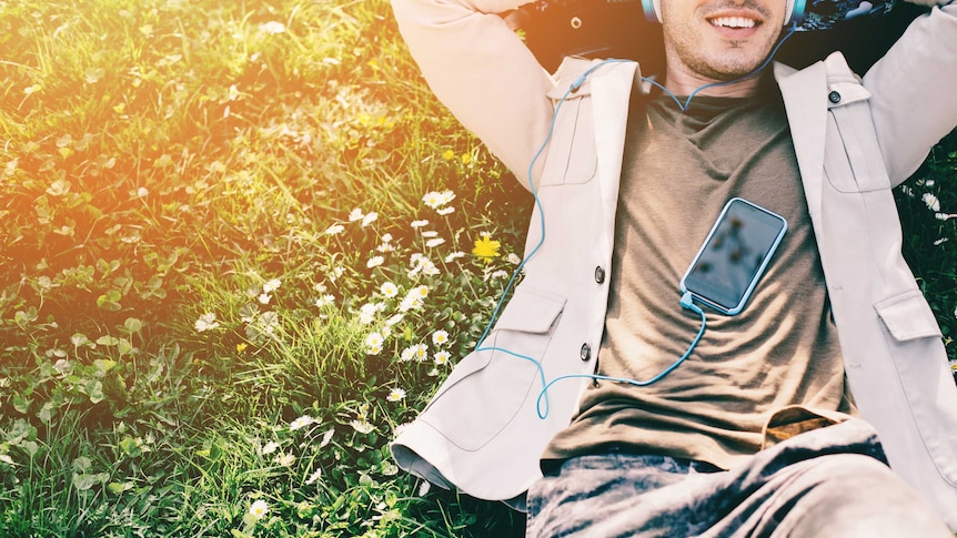 A smiling man wearing headphones plugged into his phone listens to an audiobook.