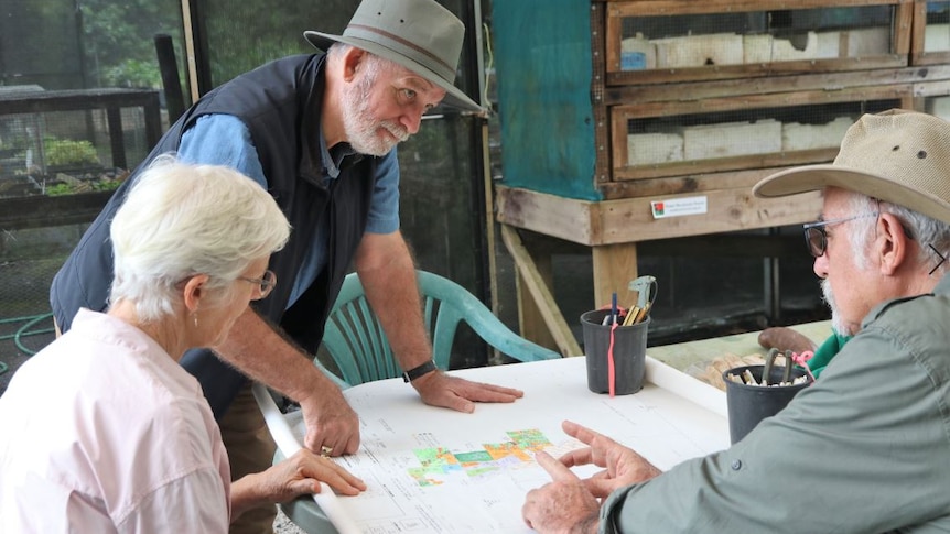 Woman and two men wearing hats sit around a large map on a table.