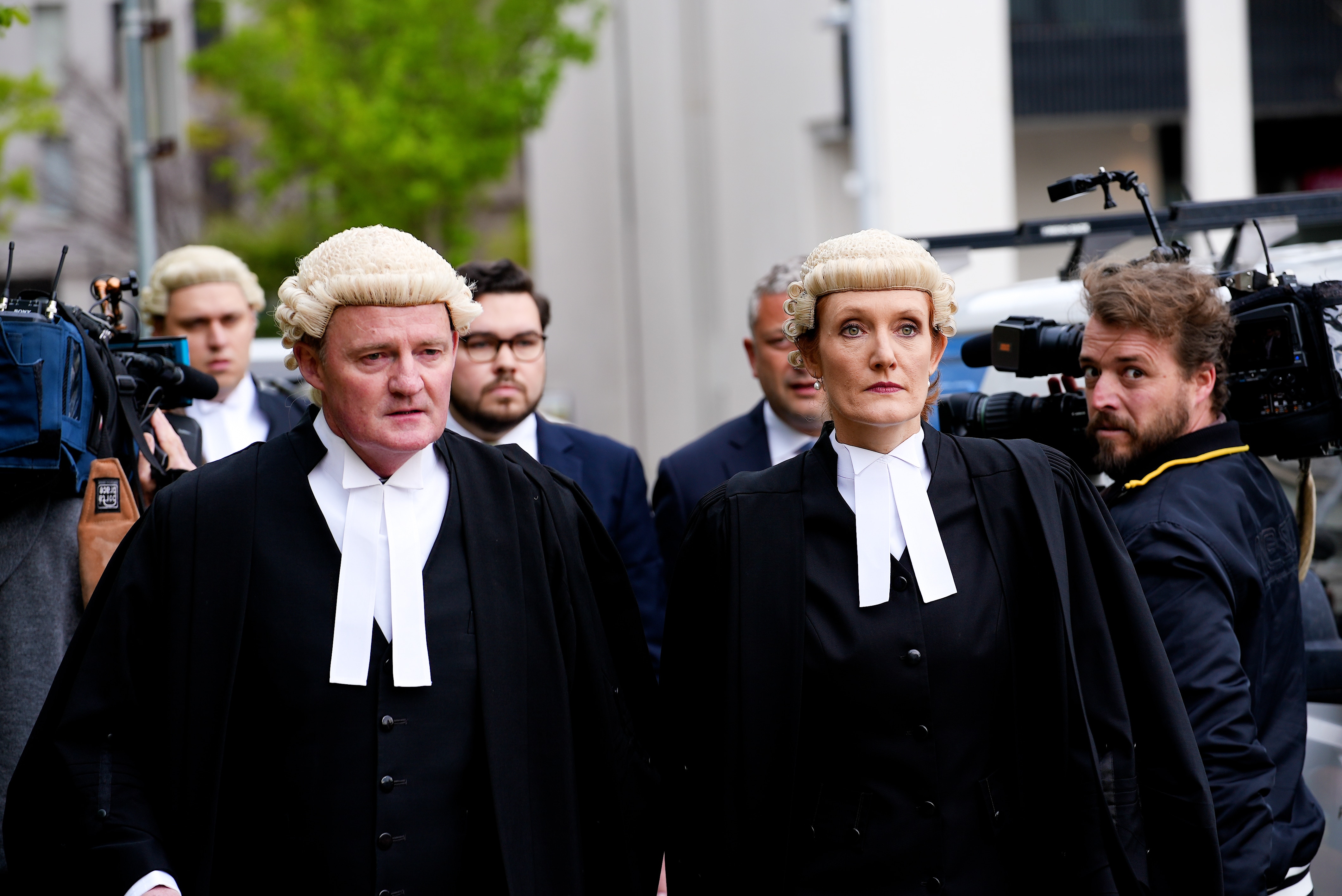 Bruce Lehrmann walks, two lawyers wearing wigs in front of him, as well as two camera operators filming.