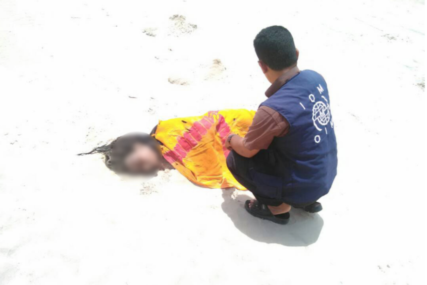 An aid worker kneels over a woman lying on a beach.