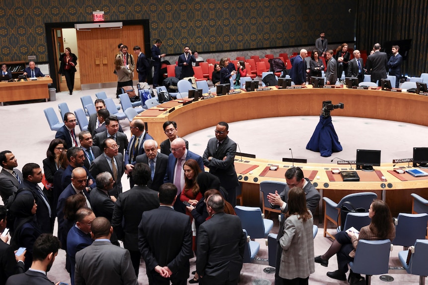 A group of people stand in a huddle near the circular UN security council table. 