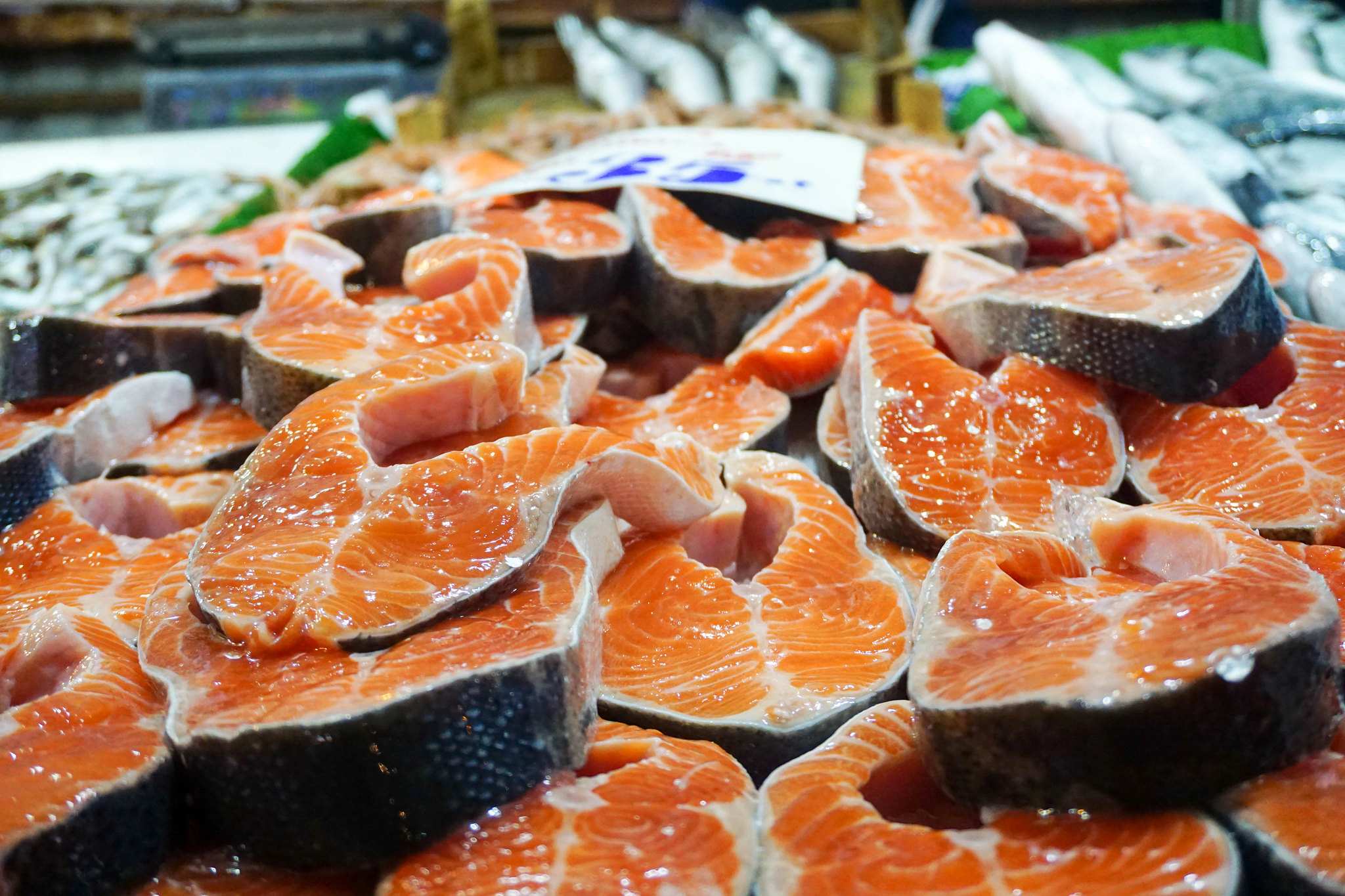 Big pieces of Norwegian salmon are stacked on top of each other in a fridge at a supermarket.
