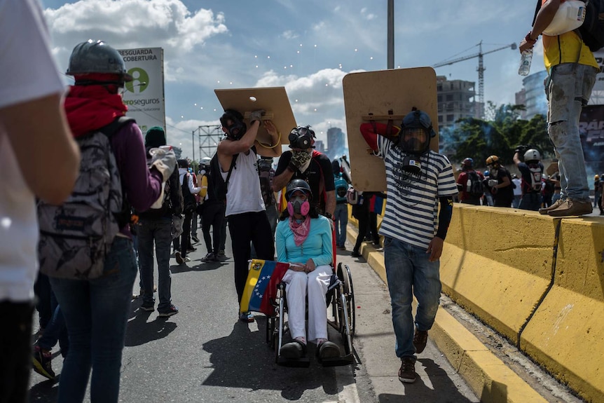 An opposition activist in a wheelchair is helped by fellow protesters