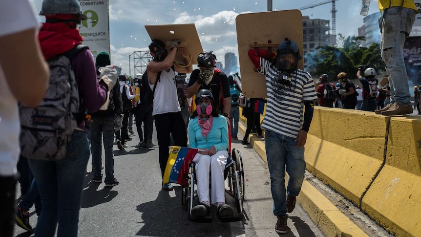 An opposition activist in a wheelchair is helped by fellow protesters