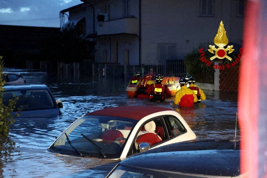A car flooded by water with emergency crews in the background 