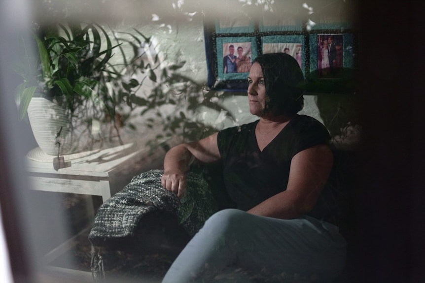 A woman sits in a darkened room.