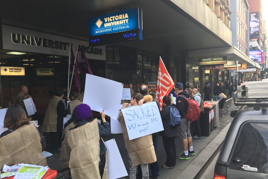 A group of protesters stand hold flags and signs outside Victoria University's city campus.