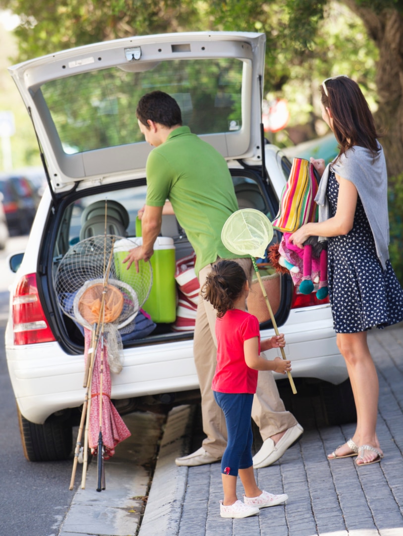 A family packs nets and umbrellas into the back of a car.