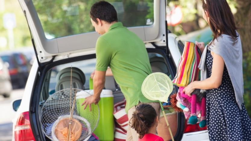 A family packs nets and umbrellas into the back of a car.