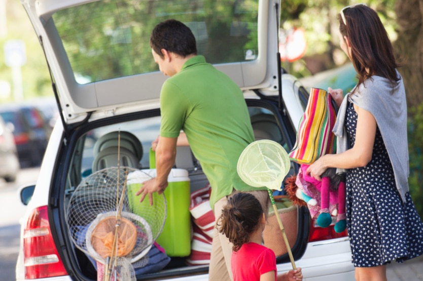 A family packs nets and umbrellas into the back of a car.