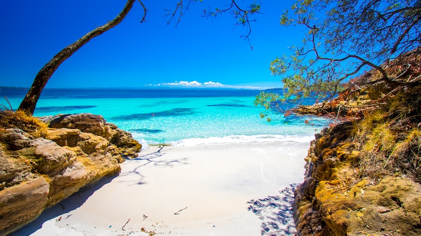 A photo looking out to a beach which has clear water and white sand