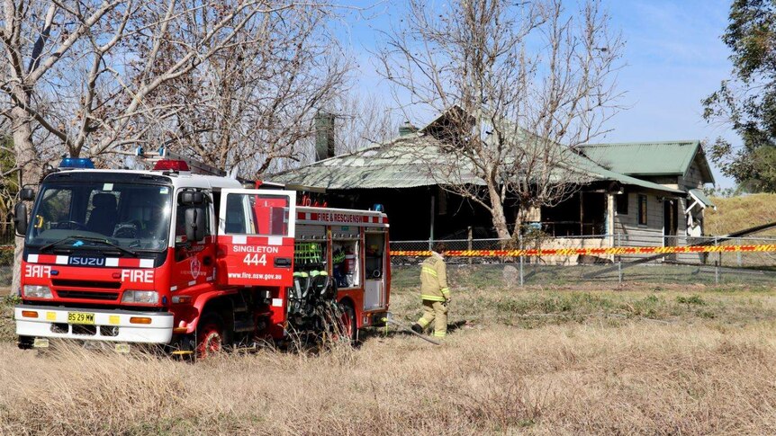 Timber cottage in a paddock completely burnt out with a fire truck in the foreground