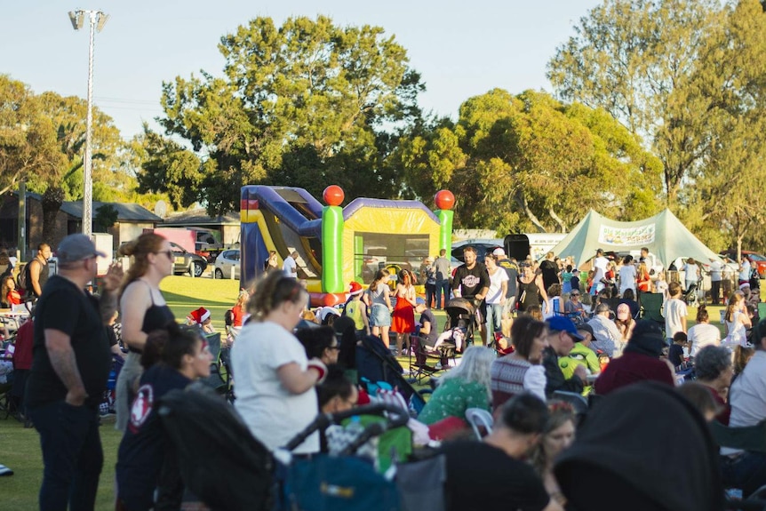 A wide shot of a Christmas event on an open green oval, in the late afternoon with families.