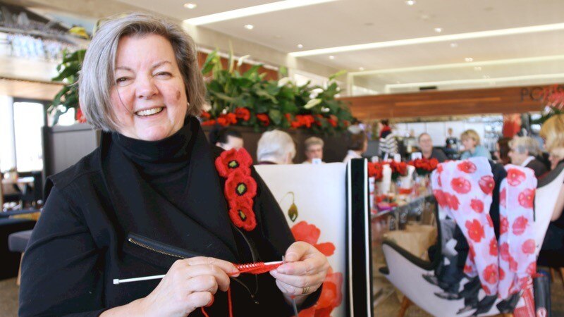 A woman smiles while knitting red poppies.