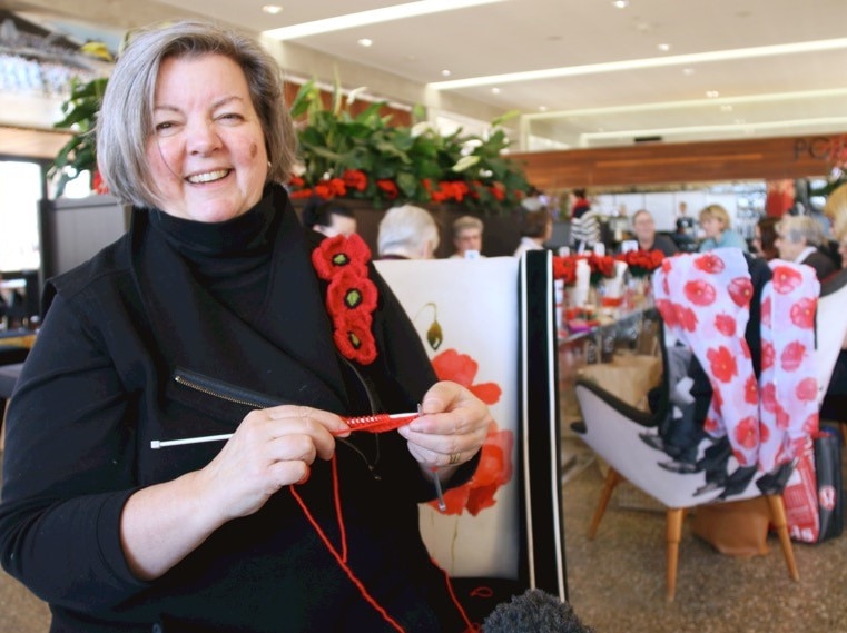 A woman smiles while knitting red poppies.