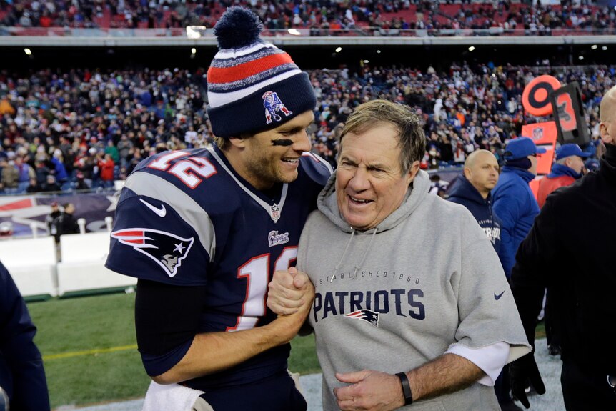 tom brady left in football gear shakes hands with belichick in a grey patriots sweater
