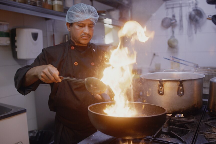 A man cooking on a large pot with fire. 
